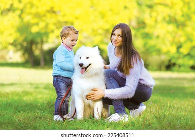 Family, Leisure And People Concept - Mother And Child Walking With Dog In Warm Sunny Day