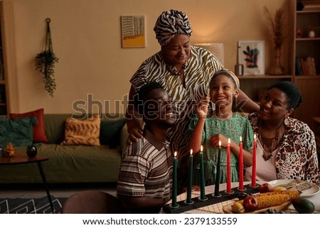 Family letting little girl to light colorful candles for Kwanzaa celebration