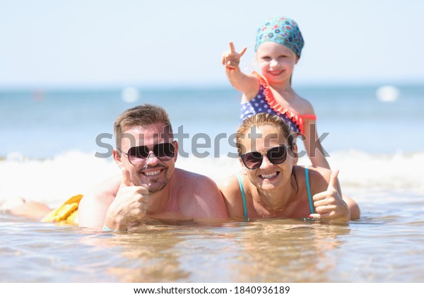 The family lies on seashore and holds thumb up.\
Family tour and travel\
concept