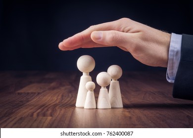 Family Life Insurance, Services And Supporting Families Concepts. Businessman With Protective Gesture And Wooden Figurines Representing Young Insured Family.