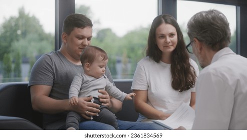 Family with little child sit on couch in clinic lobby area after doctors appointment. Doctor speaks about medical test results, gives papers. Waiting room in modern medical center. Healthcare. - Powered by Shutterstock