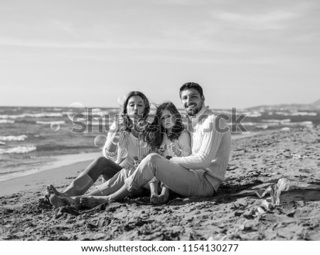 Family with little daughter resting and having fun making soap bubble at beach during autumn day