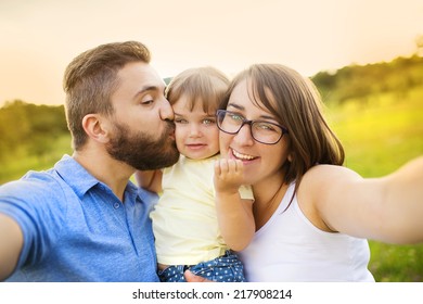 Family With Little Girl In Park Taking Selfie By Mobile Phone