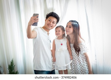 Family with little girl in park taking selfie by mobile phone. Backlit shot - Shutterstock ID 374982406