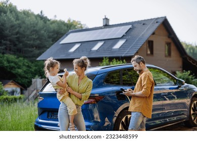 Family with little girl standing in front of their house with solar panels on the roof, having electric car. - Powered by Shutterstock