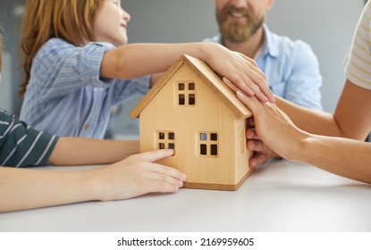 Family With Little Kids Planning To Move, Relocate, Buy New Home, Take Loan, Refinance Mortgage, Or Get Insurance. Group Of Mom, Dad And Sons Together Holding Small, Miniature Wooden House, Closeup