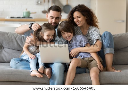 Family with little kids spend time together seated on couch in living room with laptop planning holidays tour booking hotels, e-commerce, apps users, shoppers choose on-line services and goods concept
