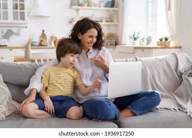 Family, Lockdown Concept. Happy Mother And Kid Son Greeting Online Looking At Web Camera Using Laptop For Video Call, Sitting On Couch At Home. Smiling Mom And Child Having Fun Talking In Video Chat.