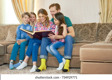 Family Looking At Photo Album. Happy People Sitting On Sofa. Family Tree Research.