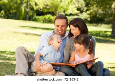 Family Looking At Their Photo Album In The Park