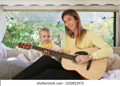 The Family Looks At The Camera And Smiles Sweetly. Mom With Beautiful White Teeth Holding A Guitar, Playing A Children's Song.