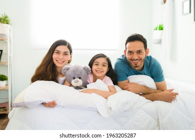 Family Love. Young Latin Mom, Dad And Elementary Girl Waking Up In Their Comfy Bed And Smiling While Making Eye Contact 