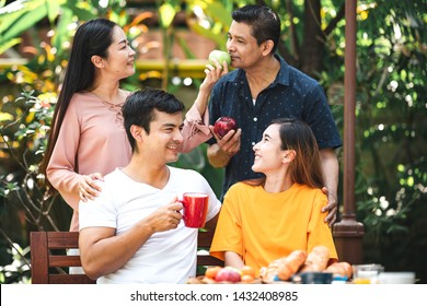 Family Lunch Outdoor. Married Mix Race Couple With Grand Parents. White Man, Asian Pregnant Woman With Senior Asian Couple In Tropical Garden.Talking And Laughing.