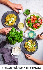 Family lunch table, top view. Peoples hands eating italian pasta with ricotta and fresh vegetables salad. Italian cuisine concept.