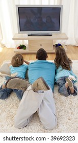 Family lying on floor in living-room watching television