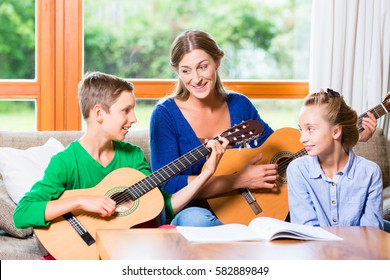 Family Making Music At Home With Guitar, Mother, Daughter And Son Playing