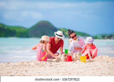 Family Making Sand Castle On White Beach. Parents And Kids Playing Together On Summer Holidays