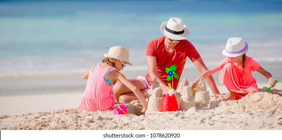 Family making sand castle at tropical white beach. Father and two girls playing with sand on tropical beach - Powered by Shutterstock