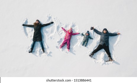 Family Making A Snow Angel. Aerial View. Mother And Father And Chilren Making A Snow Angel