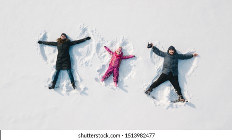 Family Making A Snow Angel. Aerial View. Mother And Father And Chilren Making A Snow Angel