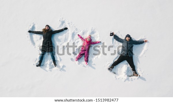 Family making a snow angel. Aerial\
view. Mother and father and chilren making a snow\
angel