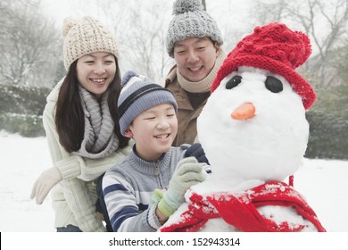 Family Making Snowman In A Park In Winter