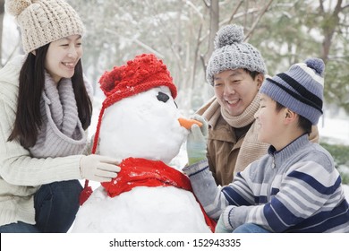 Family Making Snowman In A Park In Winter