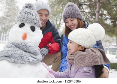 Family Making Snowman In A Park In Winter