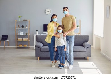 Family In Medical Masks On The Face Looks At The Camera While Standing In The Room At Home.