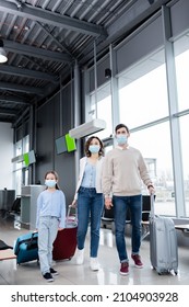 Family In Medical Masks Walking With Suitcases In Airport Lounge