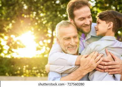 Family Meeting. A Man And A Boy Came To See His Grandfather, Who Is Sitting In A Park On A Wheelchair. The Old Man, His Son And Grandson Embrace, They Are Happy