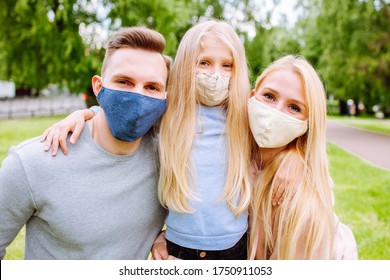 Family Members Embracing Each Other, Smiling In The Camera Wearing Cloth Face Masks. Father, Mother And Daughter Protect Themselves From The Virus.