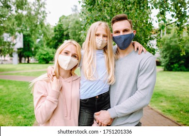 Family Members Embracing Each Other, Smiling In The Camera Wearing Cloth Face Masks. Father, Mother And Daughter Protect Themselves From The Virus