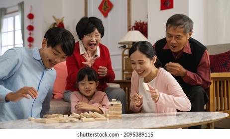 Family Members Laughing At Young Mother As She Makes Toy Wood Blocks Fall. Big Family Enjoying Tumbling Tower Game During Spring Festival. Translation Of Chinese Text: Spring