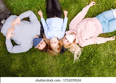 Family Members Lying On A Grass Close Each Other, Smiling In The Camera Wearing Cloth Face Masks. Father, Mother And Daughter Protect Themselves From The Virus.