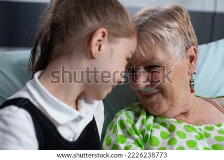 Family members smiling happily at sanatorium nursing home. Girl showing affection to elderly patient with breathing aids in hospital room. Grandmother grateful for granddaughter visit at medical