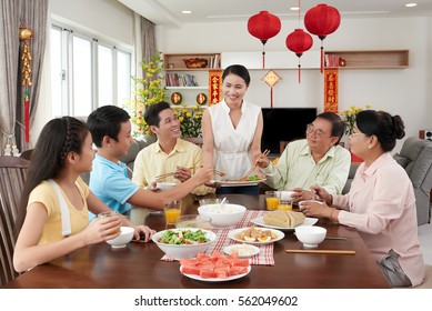 Family members taking spring rolls from dish at Tet celebration; couplets with best wishes for coming year in the background