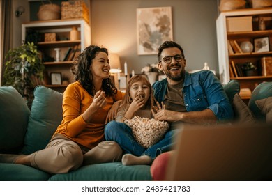 Family, mom dad and daughter holding a popcorn pot and laughing while watching a TV