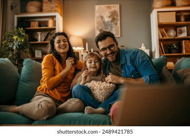 Family, mom dad and daughter holding a popcorn pot and laughing while watching a TV - Powered by Shutterstock