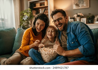 Family, mom dad and daughter holding a popcorn pot and laughing while watching a TV - Powered by Shutterstock