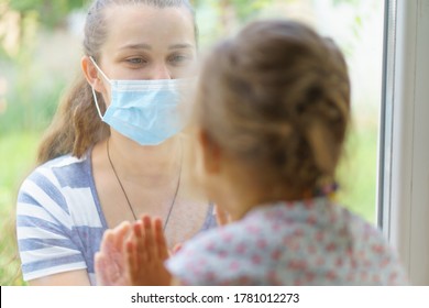 Family Mom And Daughter In Medical Mask.Young Happy Woman And Child Little Boy Sitting By The Window In Protective Masks Against The Virus. Baby Holding Hand On Glass. Mom Strokes The Baby's Face