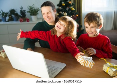 Family Mom And Two Kids With A Christmas Gift Using A Laptop Communicates With Their Friends On Video Call Using Webcam.  Stays At Home For Christmas Holidays.