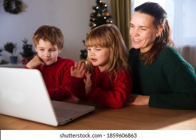 Family Mom And Two Kids Looking At Laptop And  Waving Hand, Video Calling Friends Or Relatives  Stays At Home For Christmas Holidays.