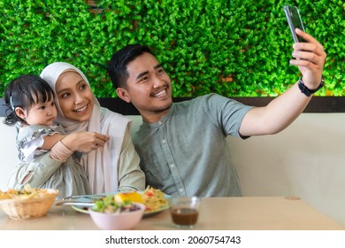 Family moment: Young couple with toddler at the restaurant taking selfie with smart phone