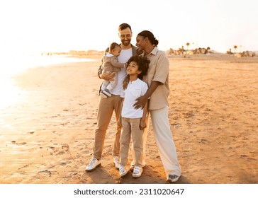 Family moments on the beach. Happy diverse parents with little kids enjoying time at sea, embracing and posing outdoors, full body length shot, free space - Shutterstock ID 2311020647