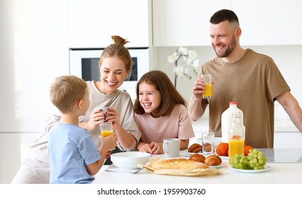 Family morning at home. Happy father, mother and two kids brother and sister enjoying time together while having healthy breakfast, drinking tea, orange juice and eating cookies in kitchen - Powered by Shutterstock