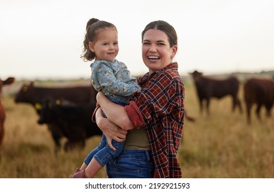 Family, Mother And Baby On A Farm With Cows In The Background Eating Grass, Sustainability And Agriculture. Happy Organic Dairy Farmer Mom With Her Girl And Cattle Herd Outside In Sustainable Nature