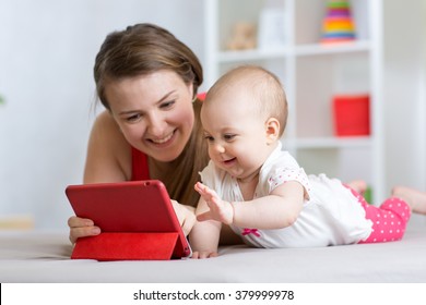 Family - mother and baby with tablet on floor at home. Woman and child girl relaxing at tablet computer.