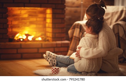 Family Mother And Child Daughter Hugs And Warm On Winter Evening By Fireplace