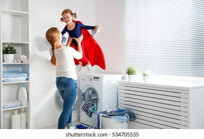 Family Mother And Child Girl Little Superhero Helper In Laundry Room Near Washing Machine And Dirty Clothes
